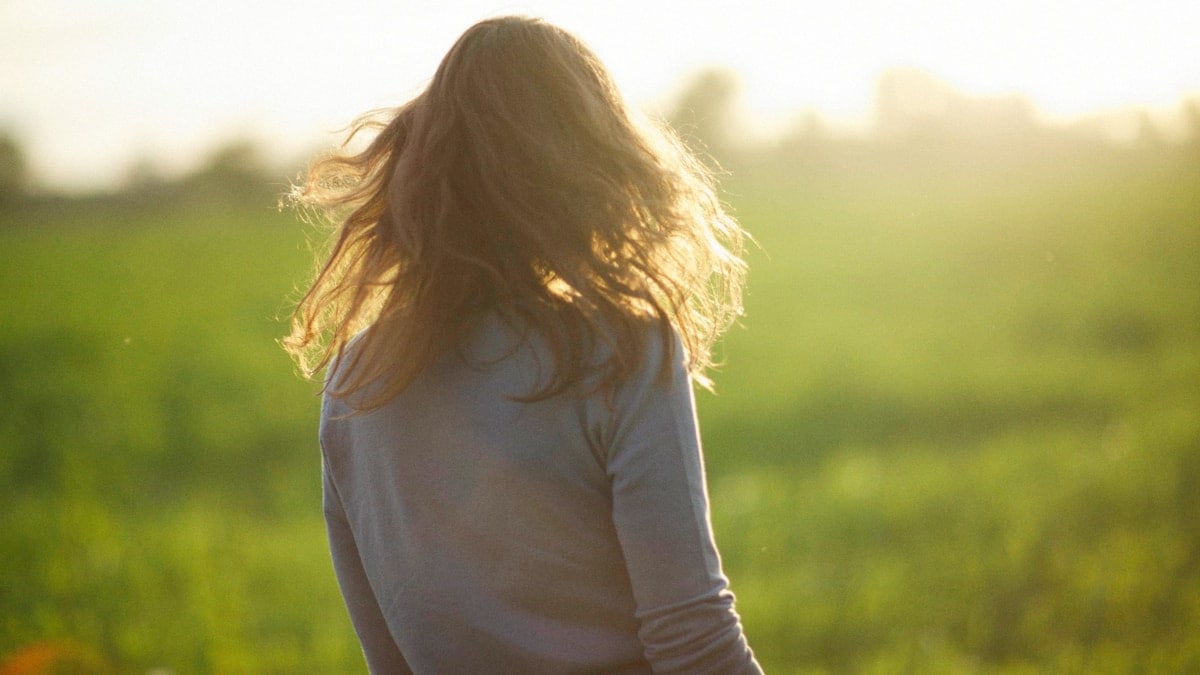a woman standing in a field with her hair blowing in the wind